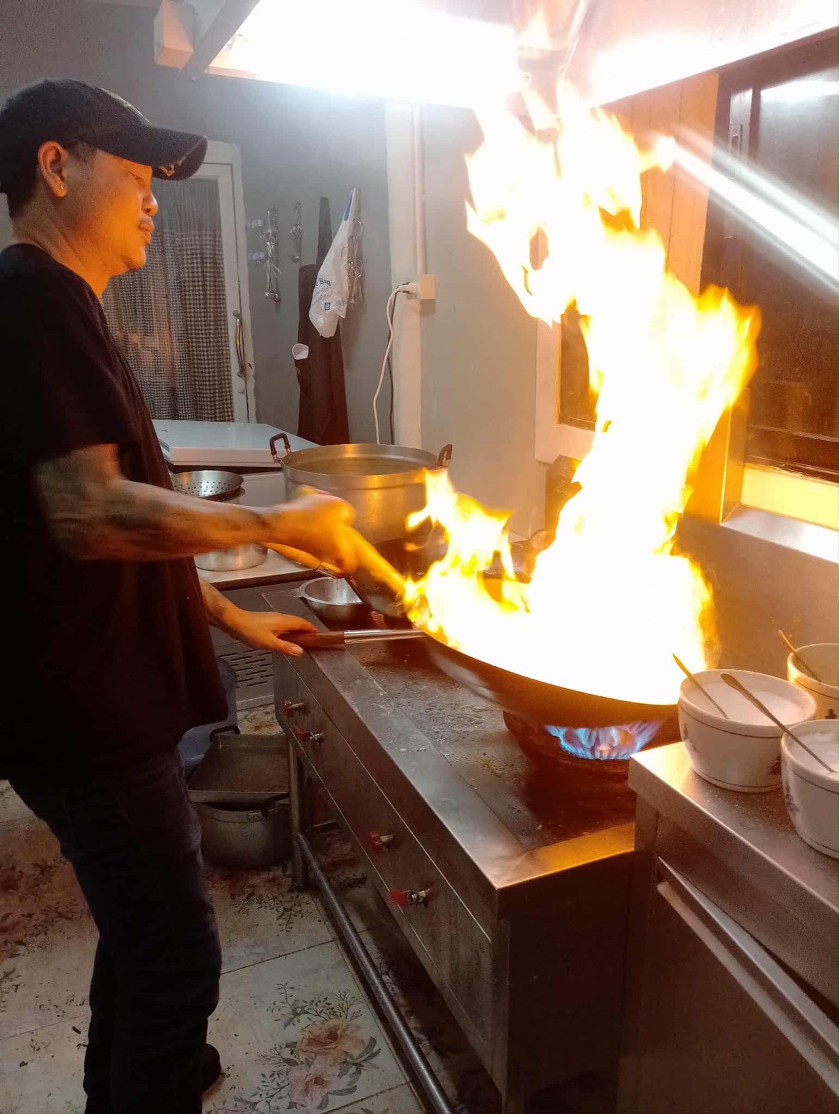 Chef Toon cuisinant au wok devant une grande flamme